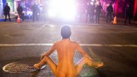A naked protester sits in front of police