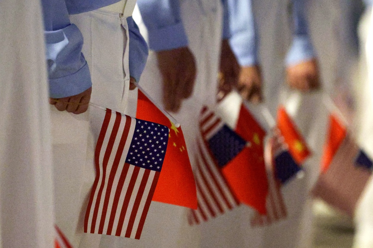 BEIJING, CHINA - MAY 13: Chinese youth hold American and Chinese flags as they join officials to welcome U.S. President Donald Trump at Beijing Capital International Airport on May 13, 2026 in Beijing, China. President Trump is meeting with President Xi Jinping in Beijing to address the Iran conflict, trade imbalances, and the Taiwan situation while establishing new bilateral boards for economic and AI oversight. (Photo by Alex Wong/Getty Images)